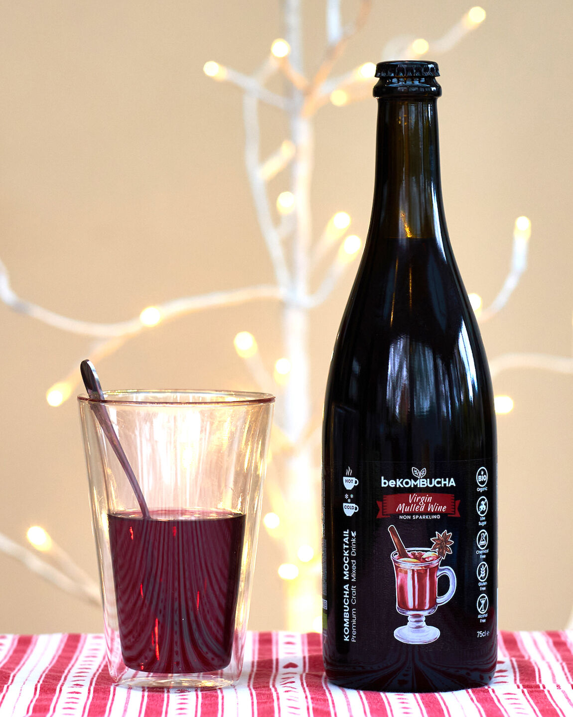 Bouteille de soda local kombucha beKOMBUCHA Virgin Mulled Wine et verre servi, sur fond de lumières festives