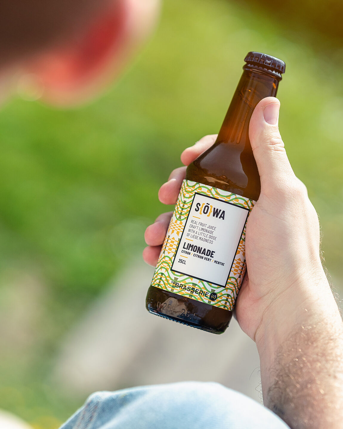 Gros plan sur une main tenant une bouteille de soda locale SÖWA en plein air